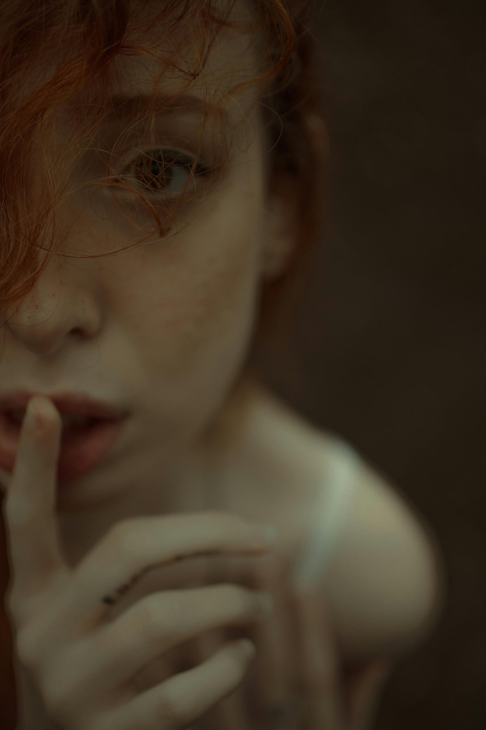 Close-up of a redhead woman with finger on lips, expressing mystery and intimacy.
