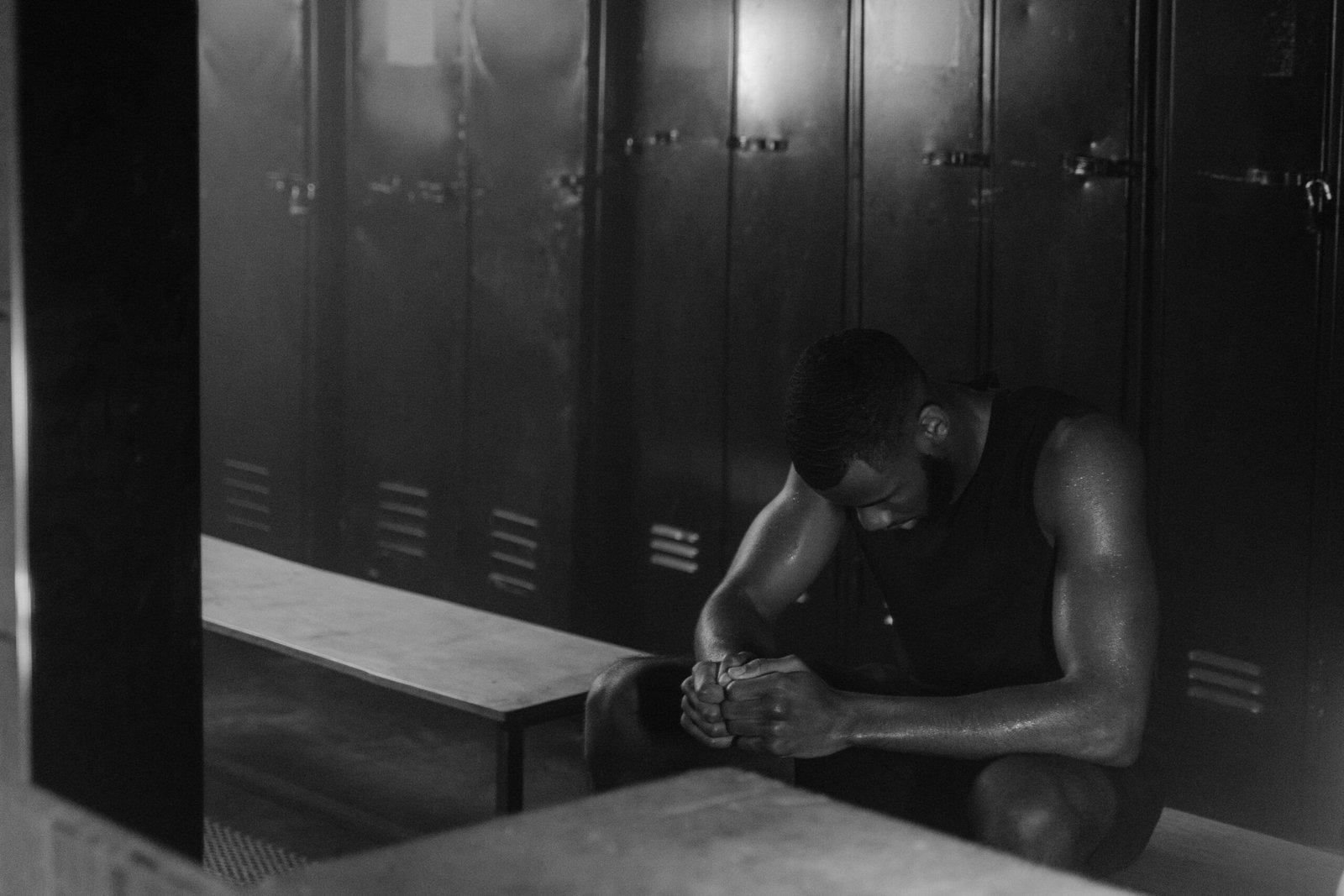 A fit African American man sits in a locker room, deep in thought.