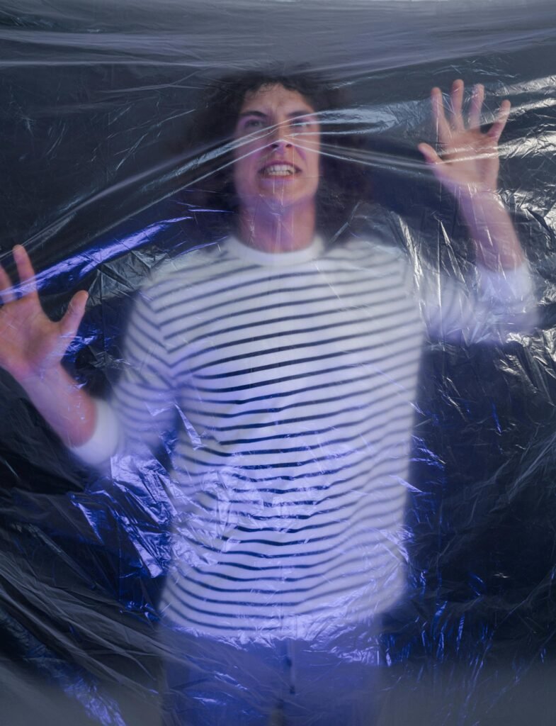 Portrait of a man pressing against plastic, symbolizing entrapment and environmental issues.